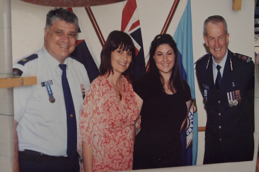 a printed-out photo of four people standing together smiling, two are in police uniforms. the photo is pegged to a board