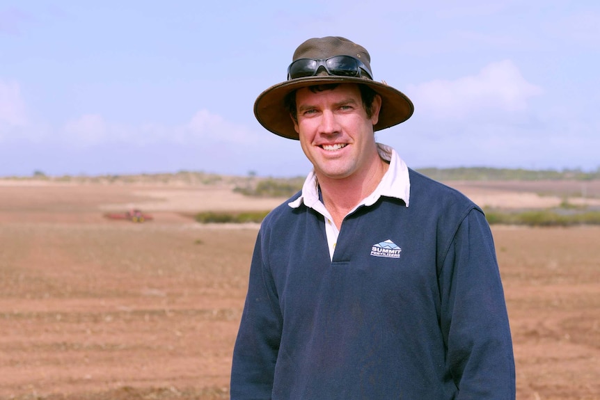 A farmer wearing a hat stands near his newly planted crop