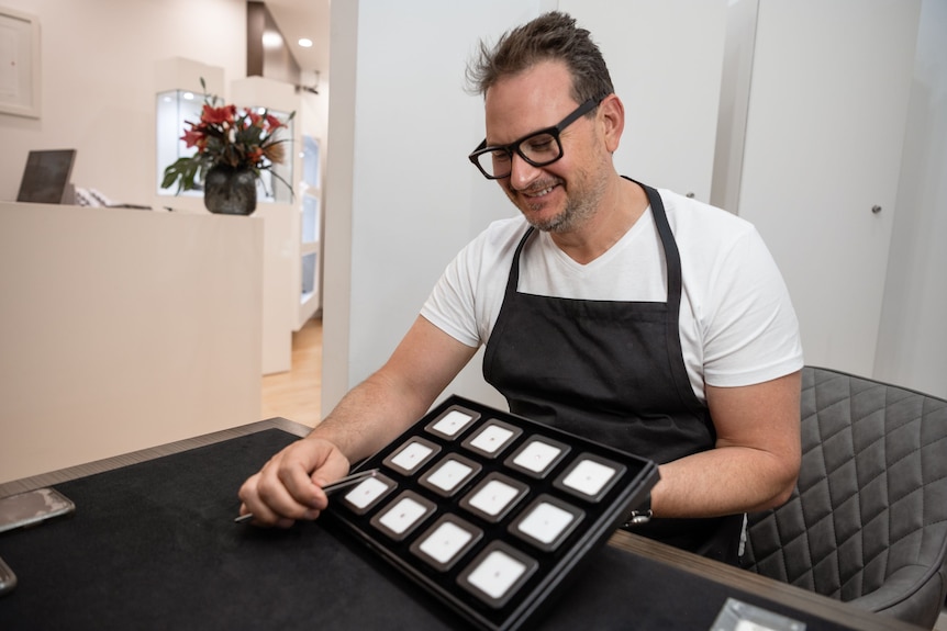 A man holds a tray of boxed jewels.