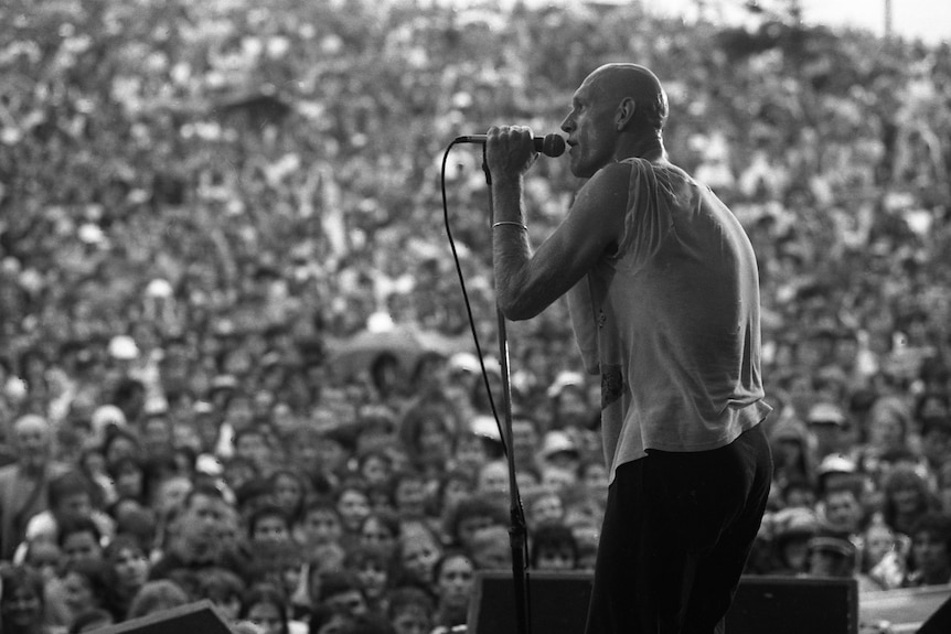 Black and white photo of a bald man singing into a microphone