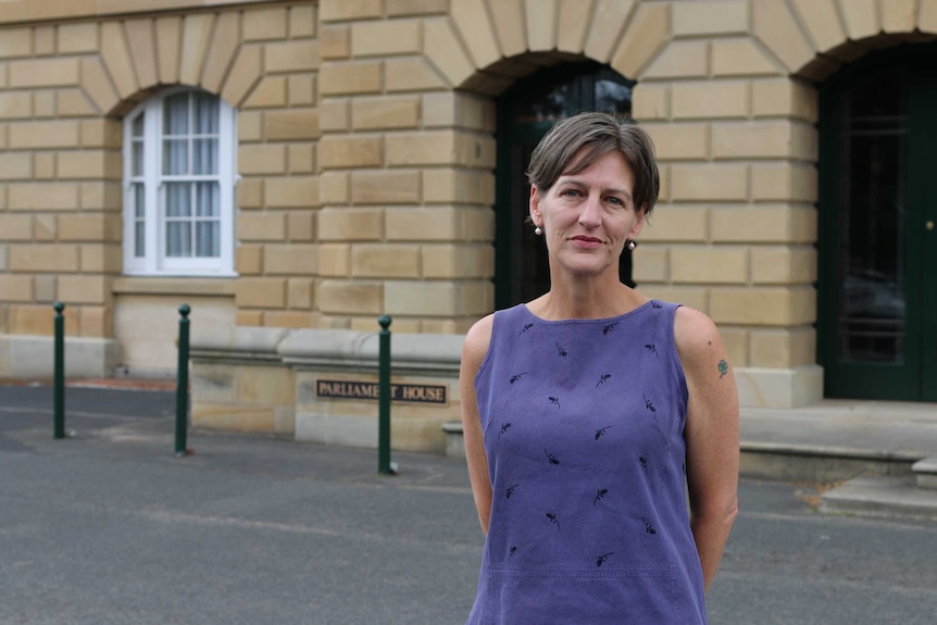 A woman in a purple top stands in front of a brick building.