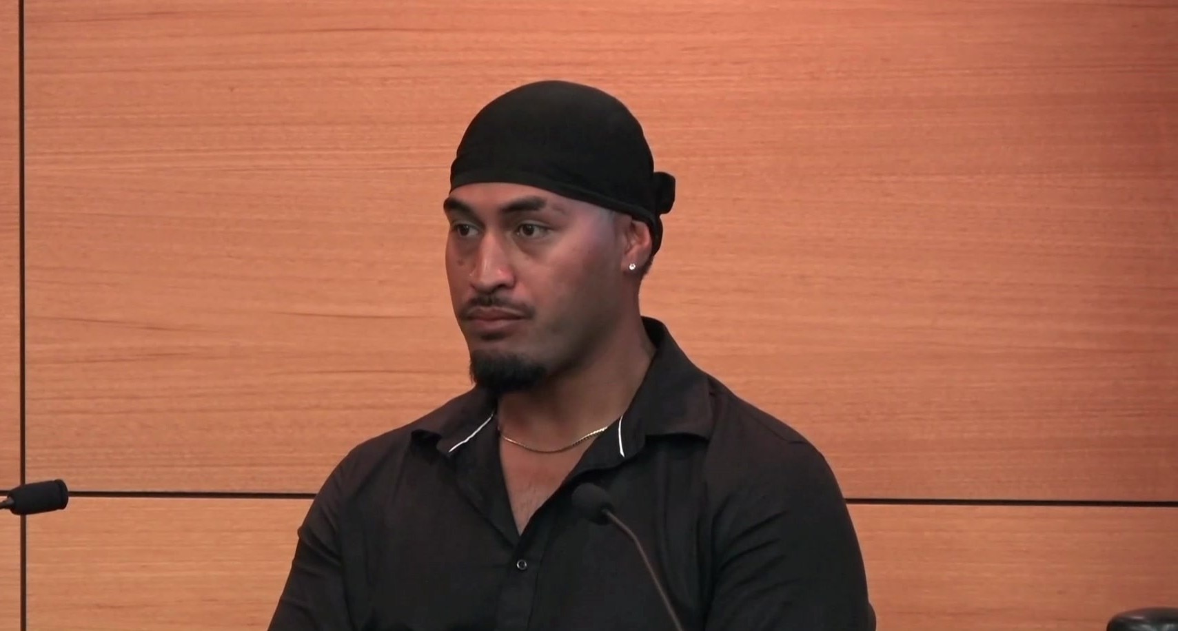 A man in a black shirt and black headband giving evidence at a lectern.