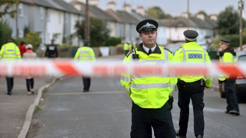 Police officers can be seen, blurred, in the foreground, as forensic officers examine a house in London.