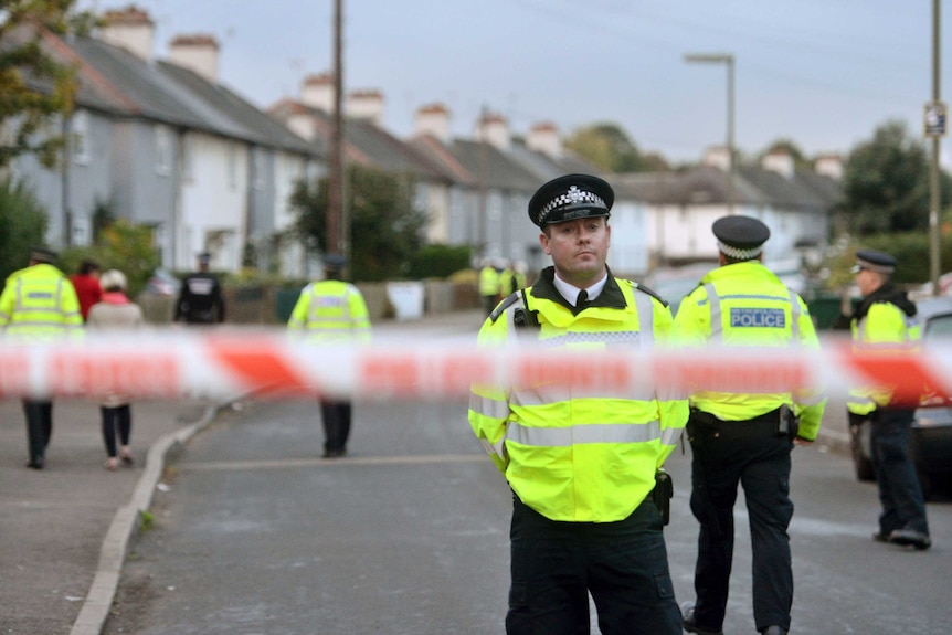 Police officers can be seen, blurred, in the foreground, as forensic officers examine a house in London.