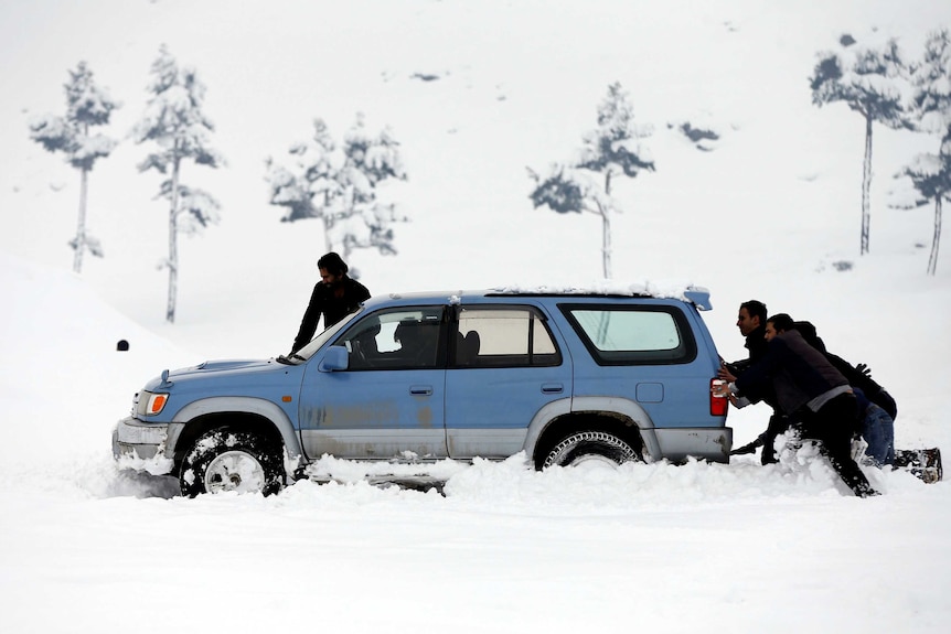 Afghan men push a car which was stuck in the snow on the outskirts of Kabul