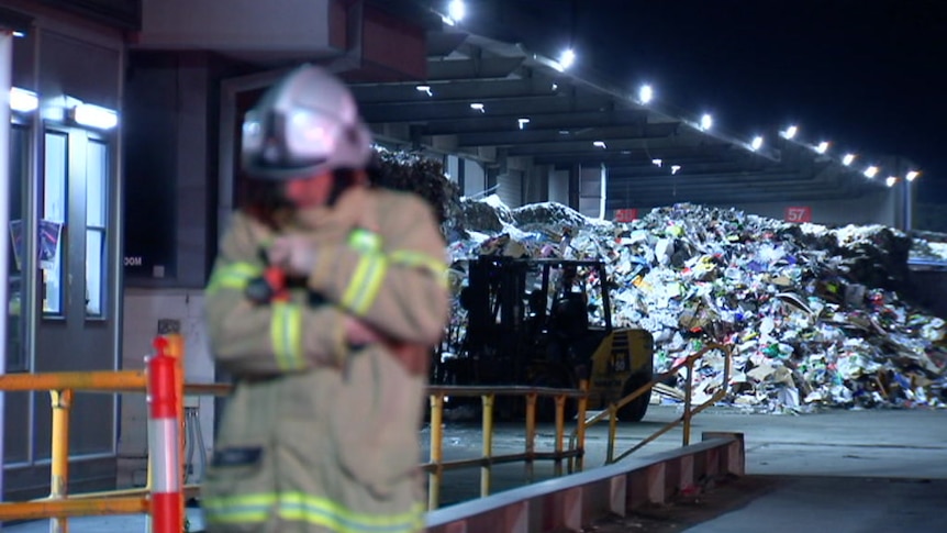 A fireman stands metres in front of a giant pile of plastic waste.
