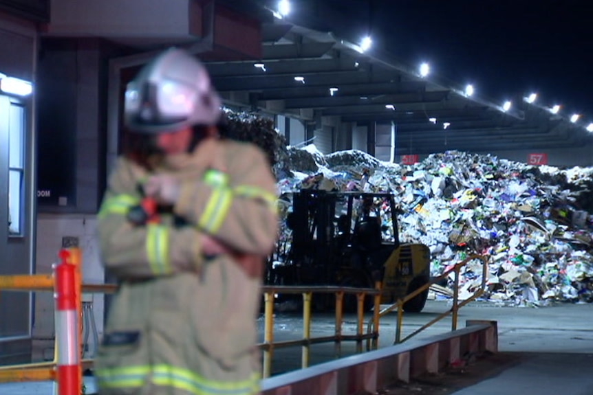 A fireman stands metres in front of a giant pile of plastic waste.