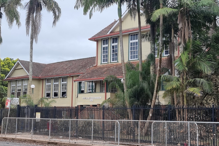 A historic weatherboard school building behind black security fencing.