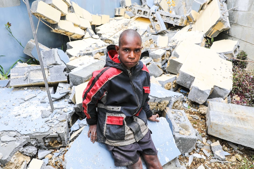 Tight shot of a young boy looking into the camera as he sits on a pile of rubble.