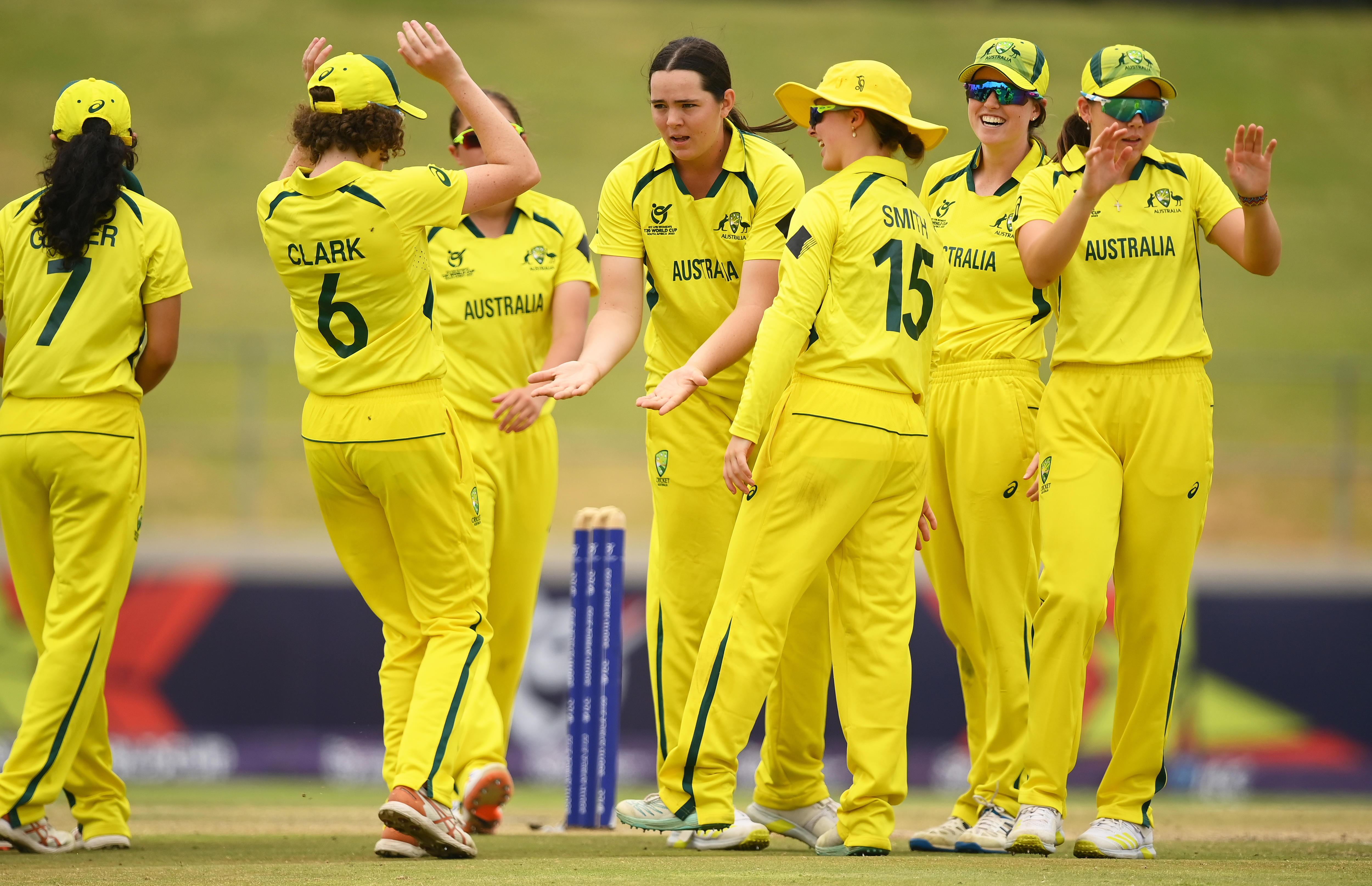 Australian cricketers in yellow and green uniforms congratulate Lucy Hamilton after taking a wicket