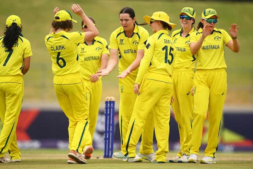 Australian cricketers in yellow and green uniforms congratulate Lucy Hamilton after taking a wicket
