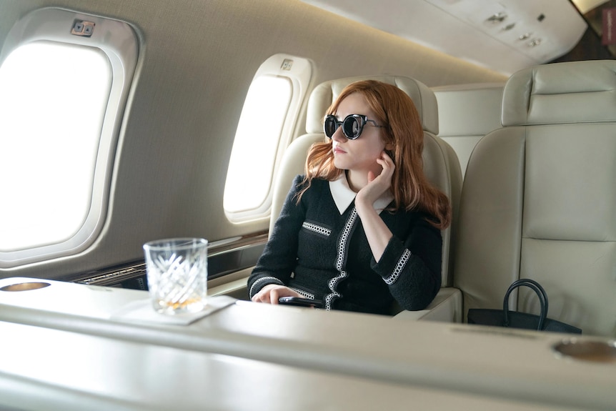 Movie still from Inventing Anna. Glamorous women in private jet looks out areophane window