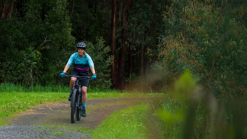 a woman rides a mountain bike on a lush green track. 