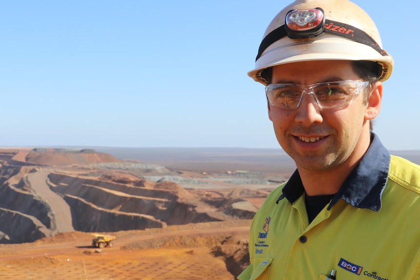 Man in the foreground left hand side in helmet and clear glasses, overlooking mine site below