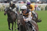 A jockey rides his horse through soft, wet ground to win a big race at Flemington.