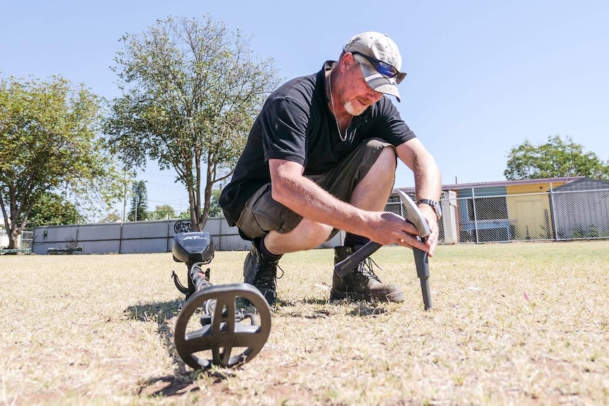 Dave Knox crouches down and uses a pin pointer to hone in on a potential target in the ground.