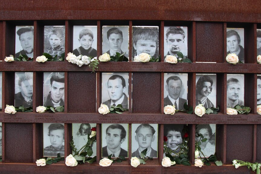 A memorial with photos of people killed at the berlin wall, many young men and boys. Roses sit in front of their photos.