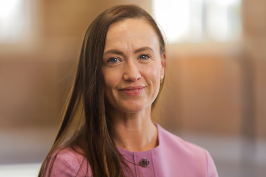 A woman with long brown hair, smiles for the camera in this head-and-shoulders photograph