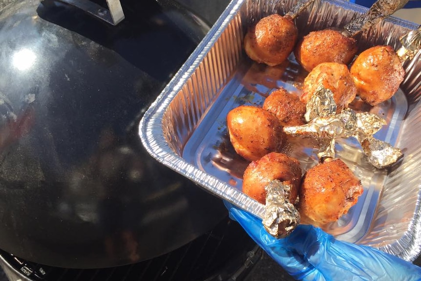 Close up of a tray of barbecued chicken drumsticks beside a barbecue smoker