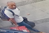 Security footage of a fit-looking man in his 30s with a shaved head walking down a street carrying luggage.