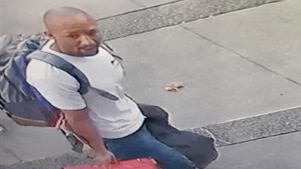 Security footage of a fit-looking man in his 30s with a shaved head walking down a street carrying luggage.