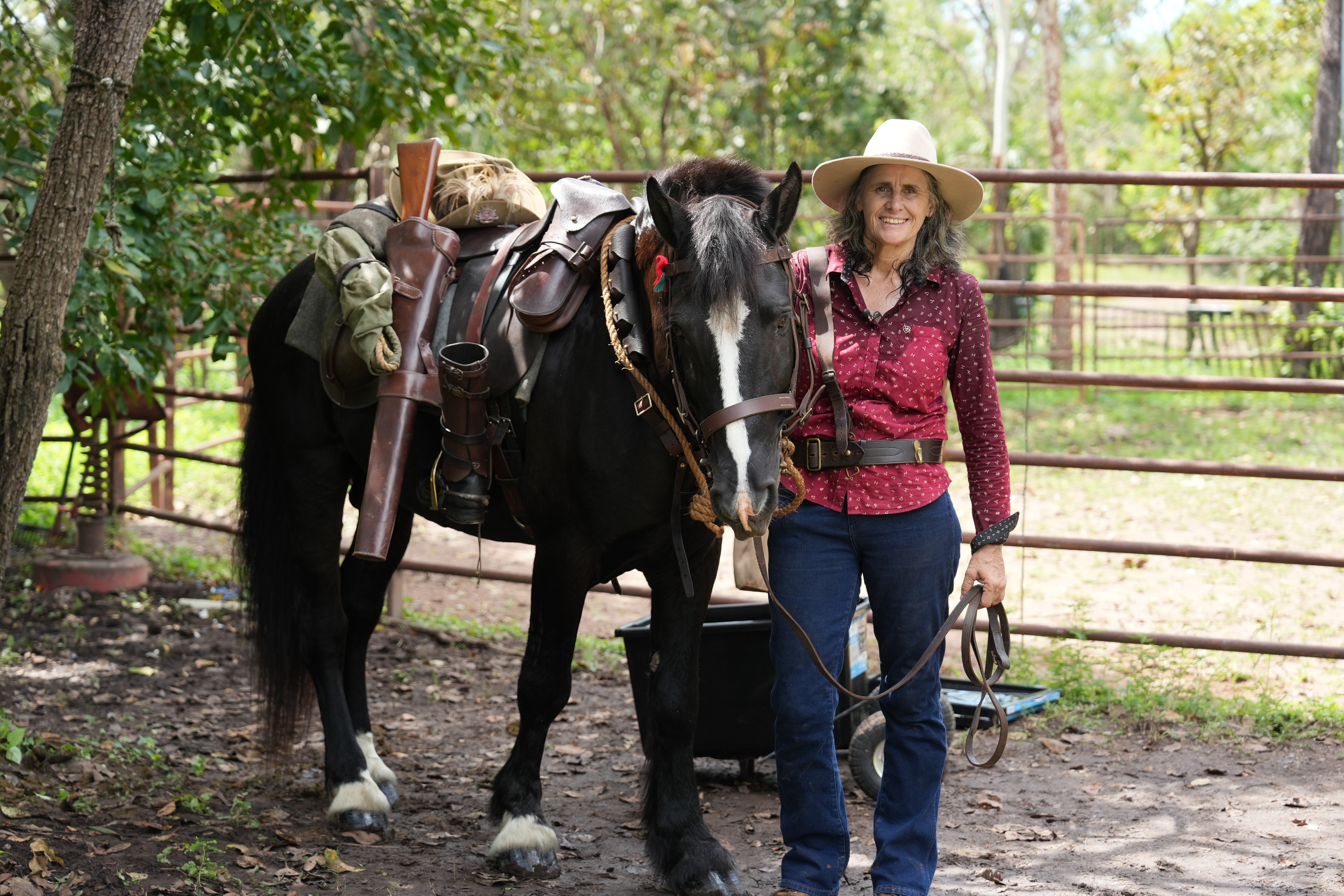 A woman, smiling widely, standing next to a horse, with a number of wartime relics attached to its saddle.