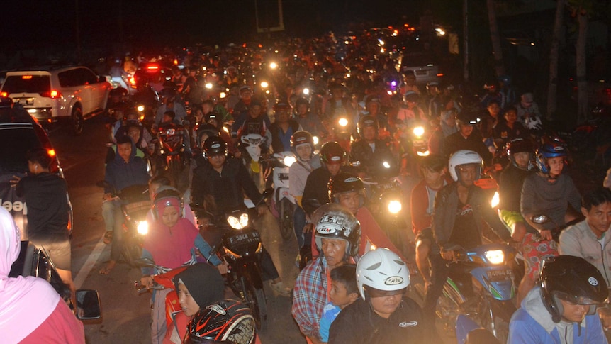A traffic jam of scooters packs a road as the headlights shine in the darkness.
