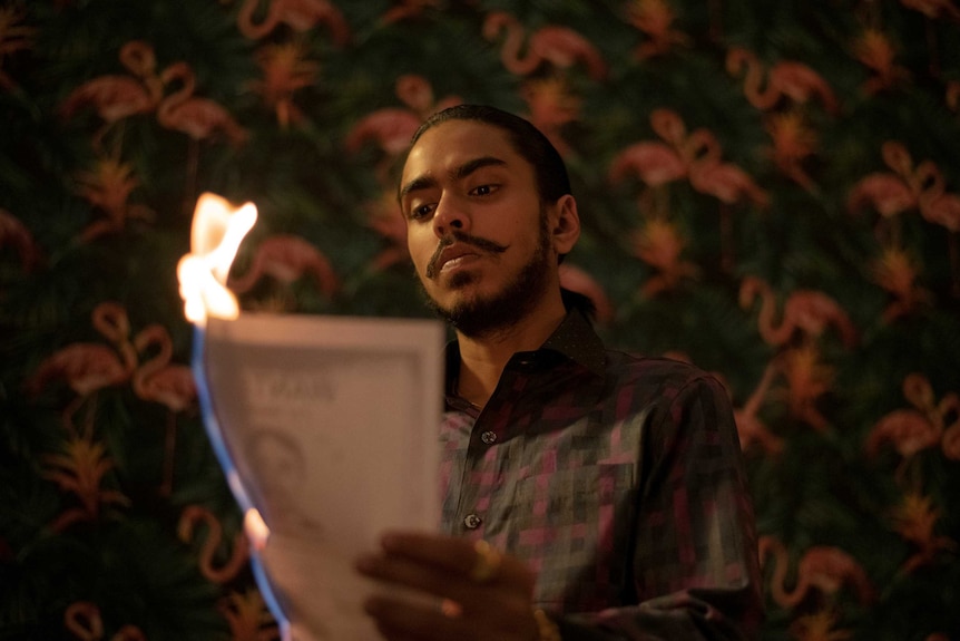 A still from the film The White Tiger with a young man burning a piece of paper