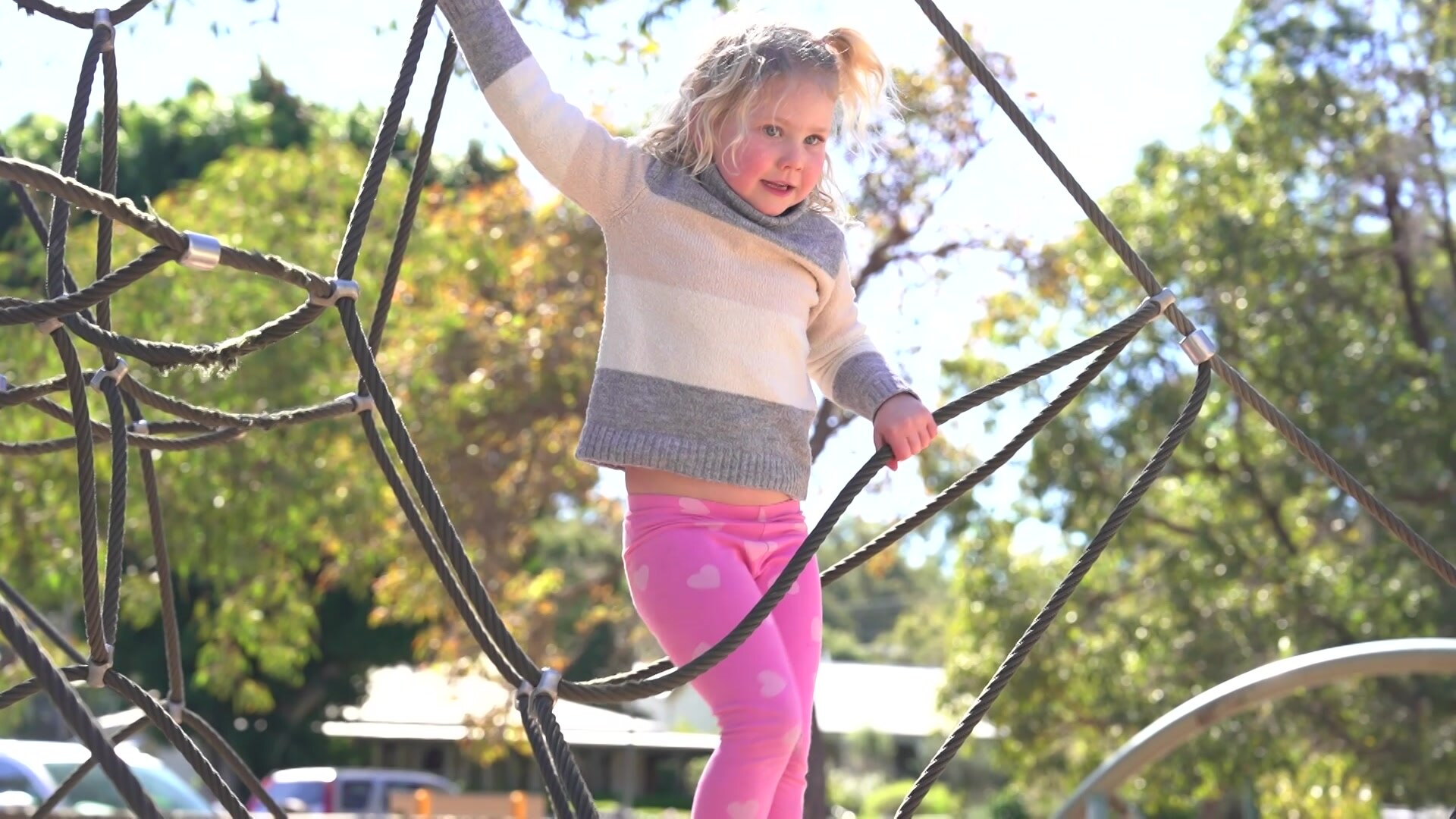 A young blonde girl plays on climbing ropes at a playground. 