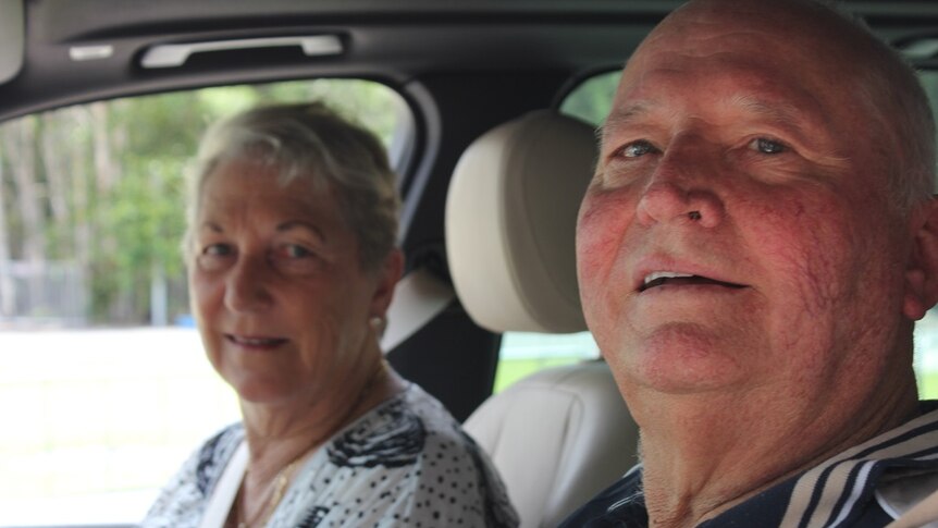 Man and woman sitting inside their car, looking at the camera.