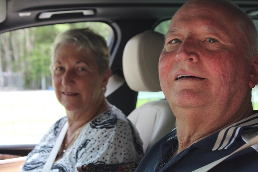 Man and woman sitting inside their car, looking at the camera.