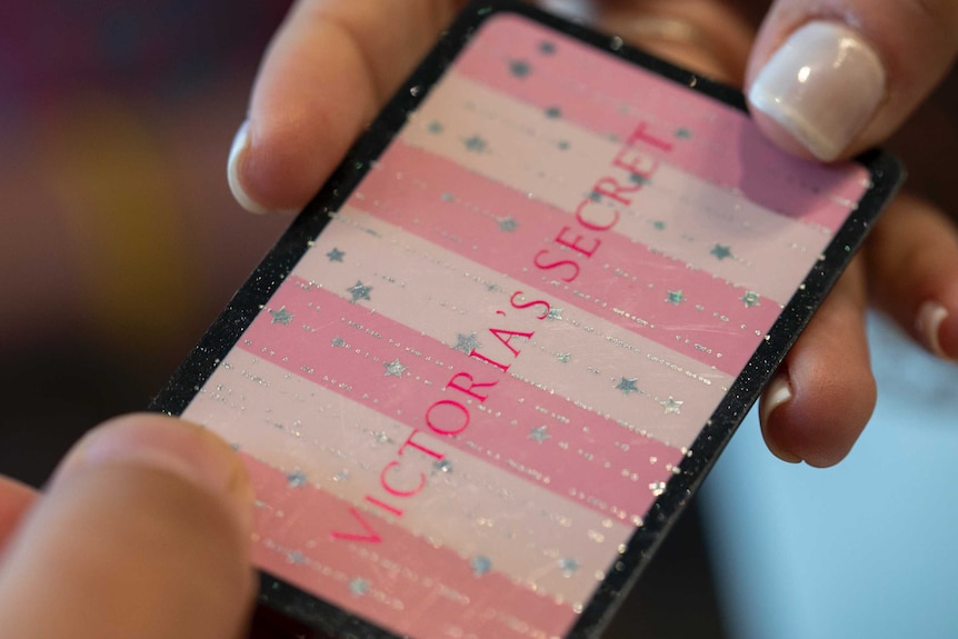 A close up shot of a white and pink card, which is covered in some small sparkles and gems, which reads 'VICTORIA'S SECRET'