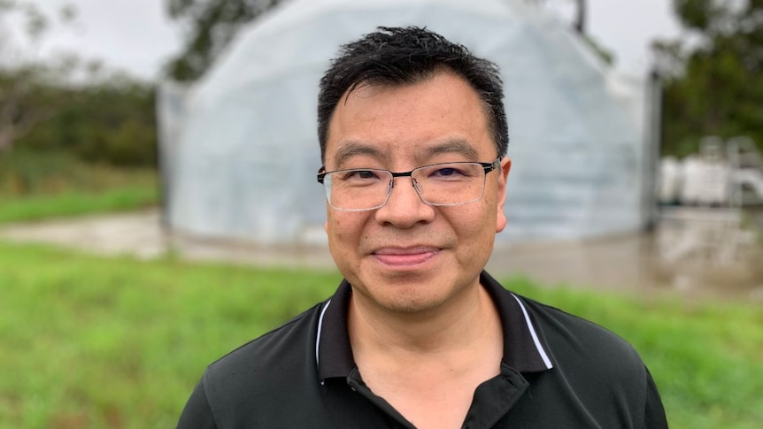 A man wearing glasses and a black polo stands in front of a dome in a garden.