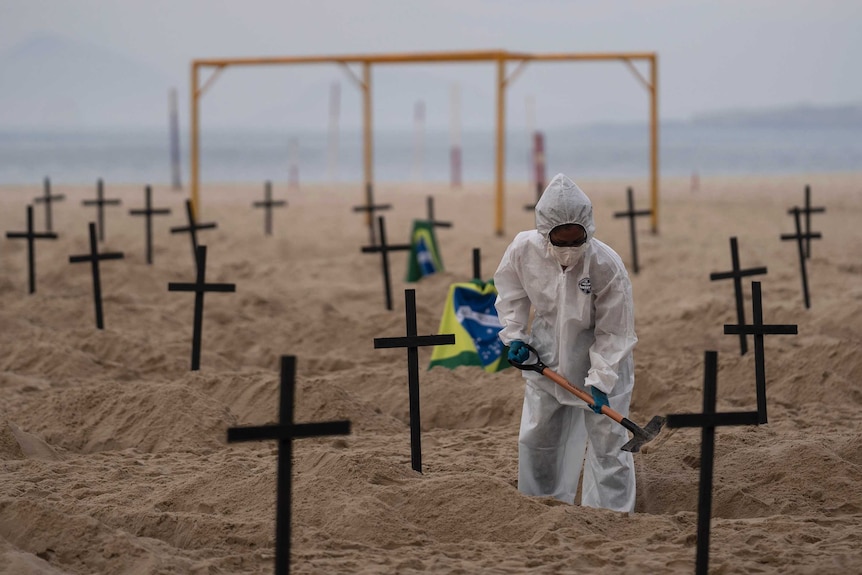 An activist in a hazmat suit digs symbolic graves on Copacabana beach during a protest against the government's COVID-19 plan.