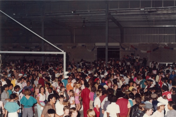 A photo from the 1990s of lots of teenagers in a shed, dancing.