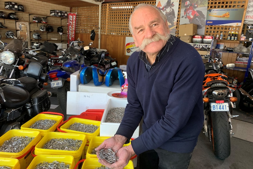 An older man with his hands full of drink can ring-pulls, surrounded by buckets of ring-pulls.