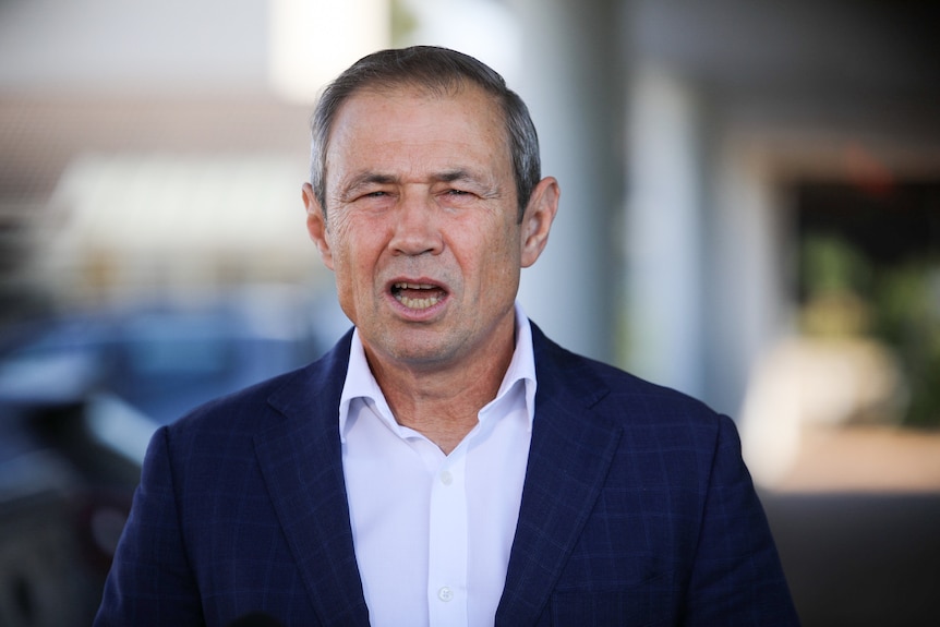 A head and shoulders shot of WA Premier Roger Cook speaking while wearing a dark blue suit and white shirt.