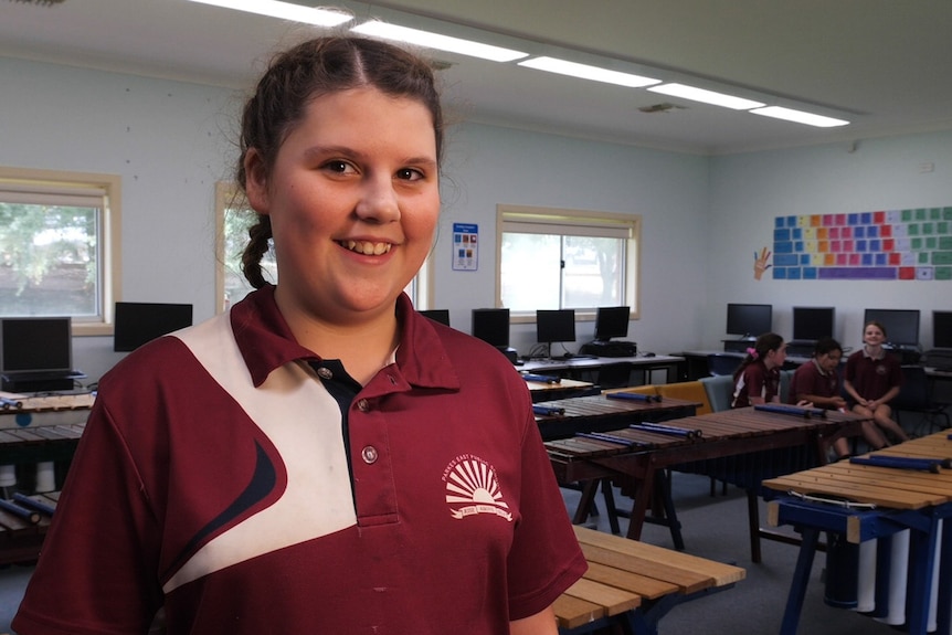 A girl in a maroon Parkes East Public School uniform standing in a room full of marimbas and computers.