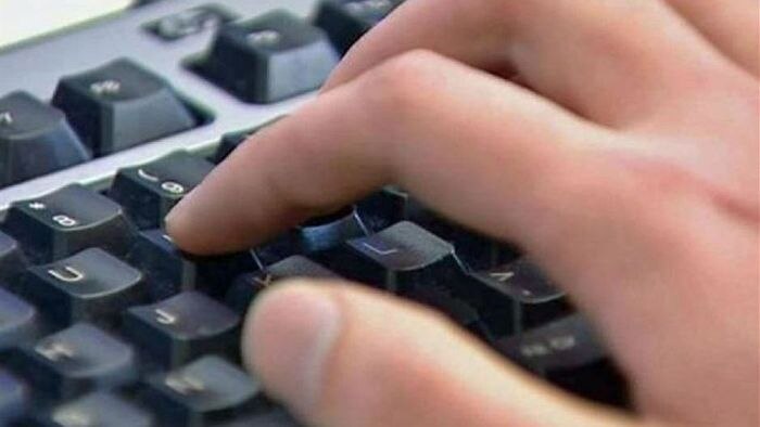 A close-up image of a hand typing on a black keyboard.