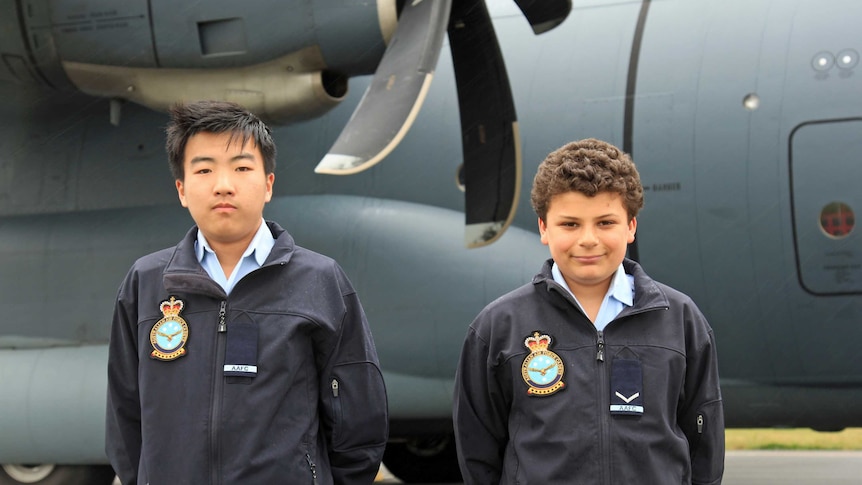 Two young teenagers standing in front of a large grey plane