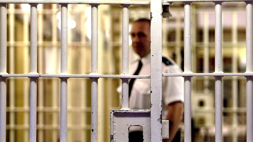 A prison guard stands behind a locked gate