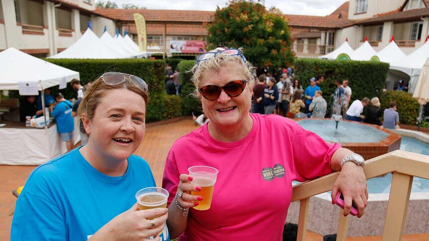 Two smiling women with ciders stand on a staircase.