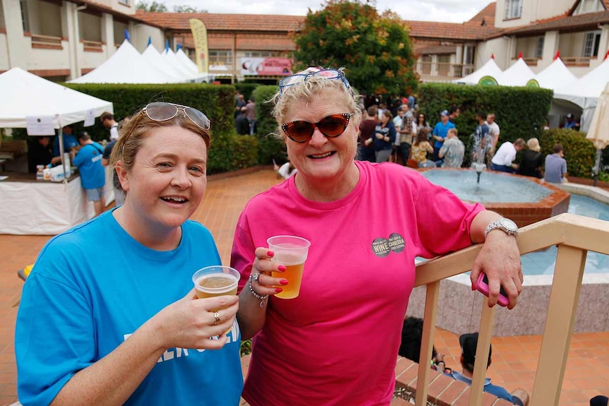 Two smiling women with ciders stand on a staircase.