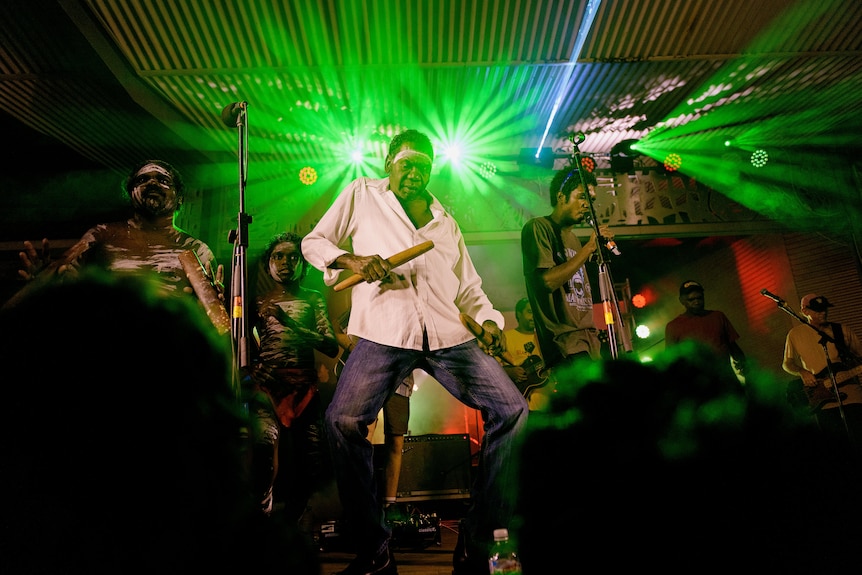 an aboriginal man dancing on stage with green lights behind him