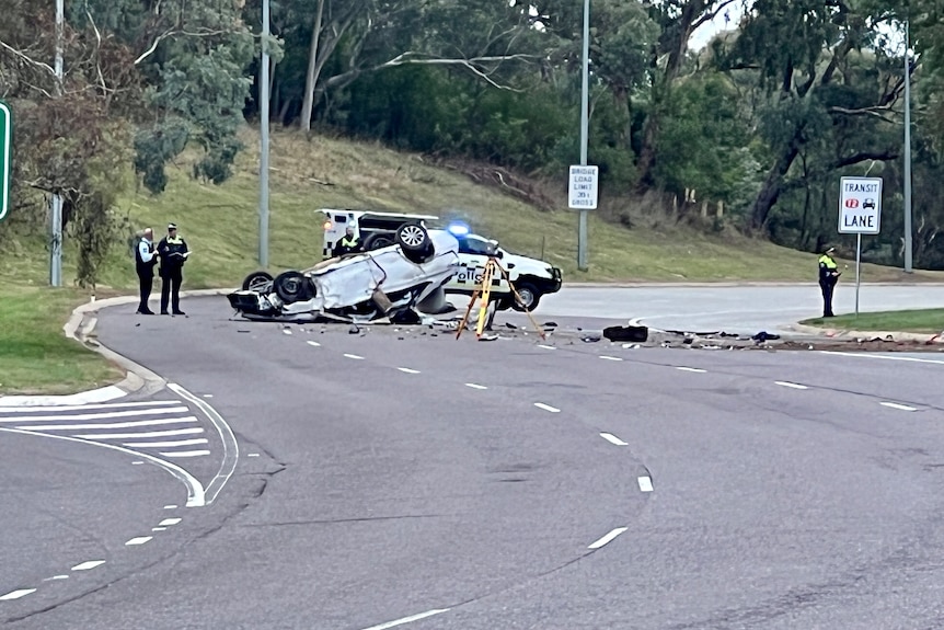 A car flipped over with debris on the road and police around it