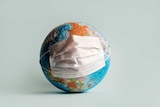 Globe made of jigsaw puzzles with a protective medical mask.