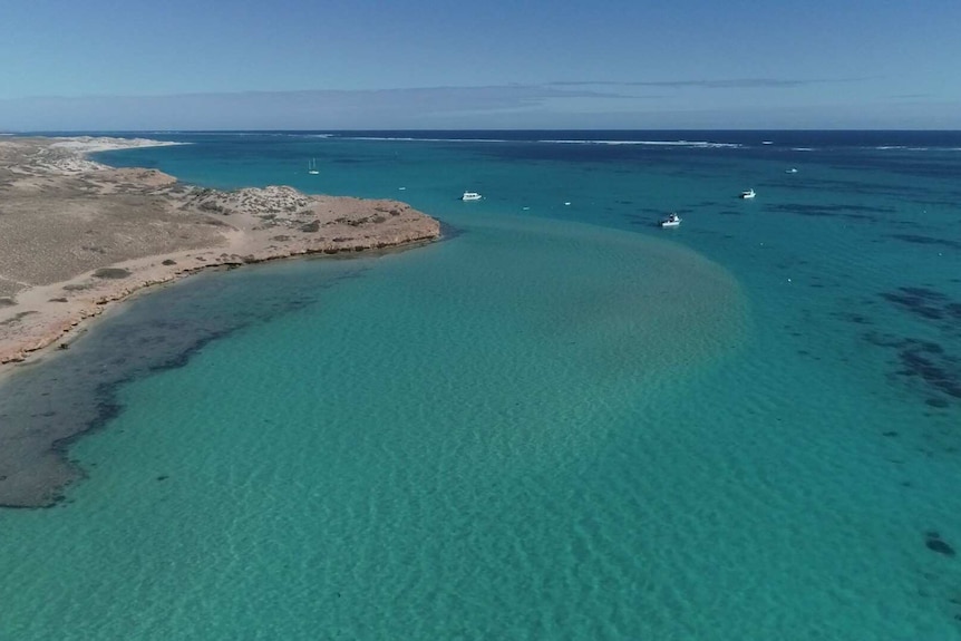 A drone shot of water off the coast of Coral Bay with the coastline visible and boats dotting the water.