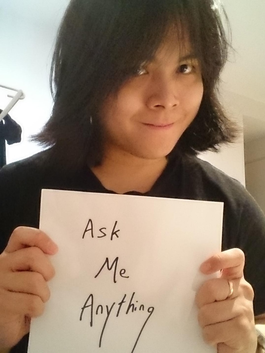 A young man with chin-length hair holds a piece of paper with 'ask me anything' written on it.