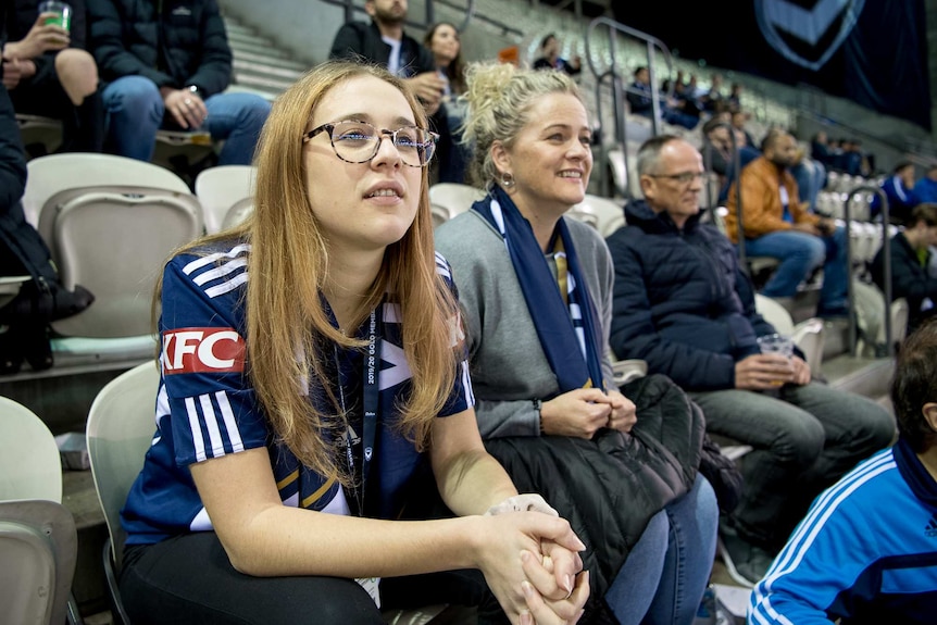 Two women look towards the field among other spectators.