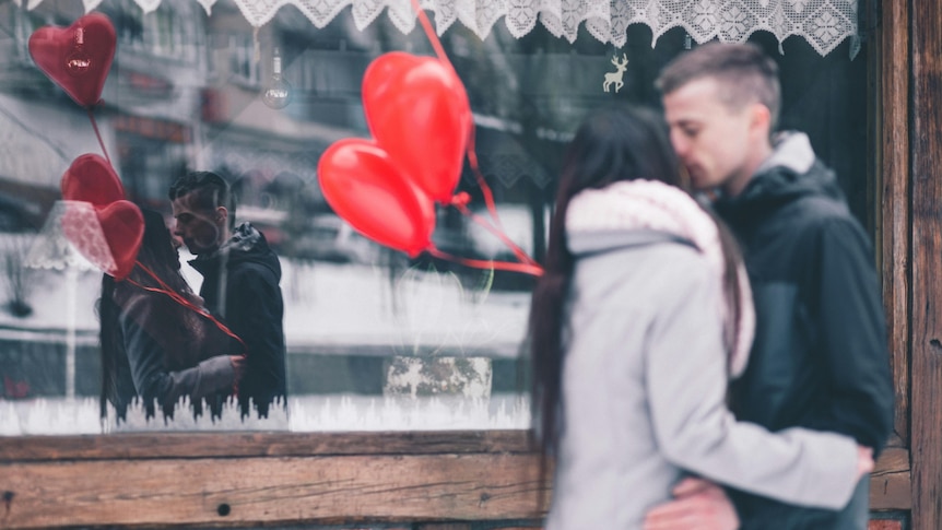A woman and a man kiss in front of a shopfront.